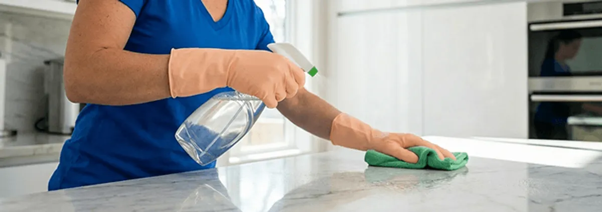 Maid service worker spraying and wiping a kitchen countertop with a microfiber cloth for sanitizing, Richmond, VA.